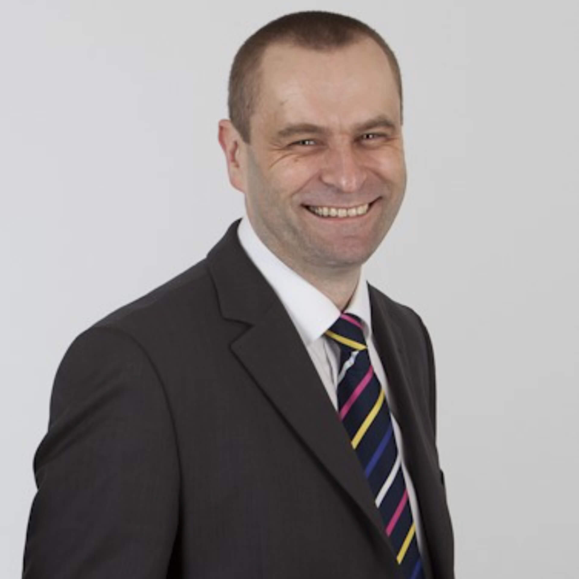 John Middleton smiling widely, wearing a black suit and colourful striped tie.